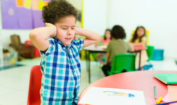 Child with hands over ears in classroom