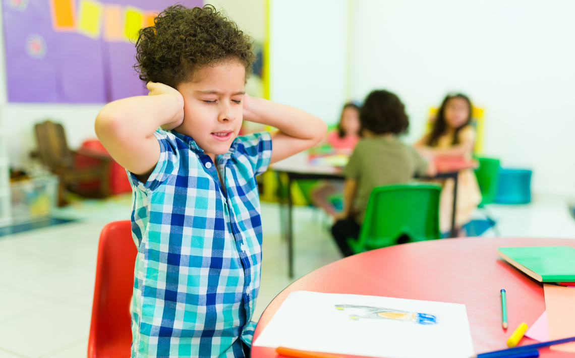 Child with hands over ears in classroom